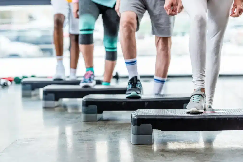 Cours de Step Fitness : Entraînement en Groupe Groupe de personnes en vêtements de sport faisant de l'aérobic ou de la musculation avec des step en salle de sport, vues des jambes.