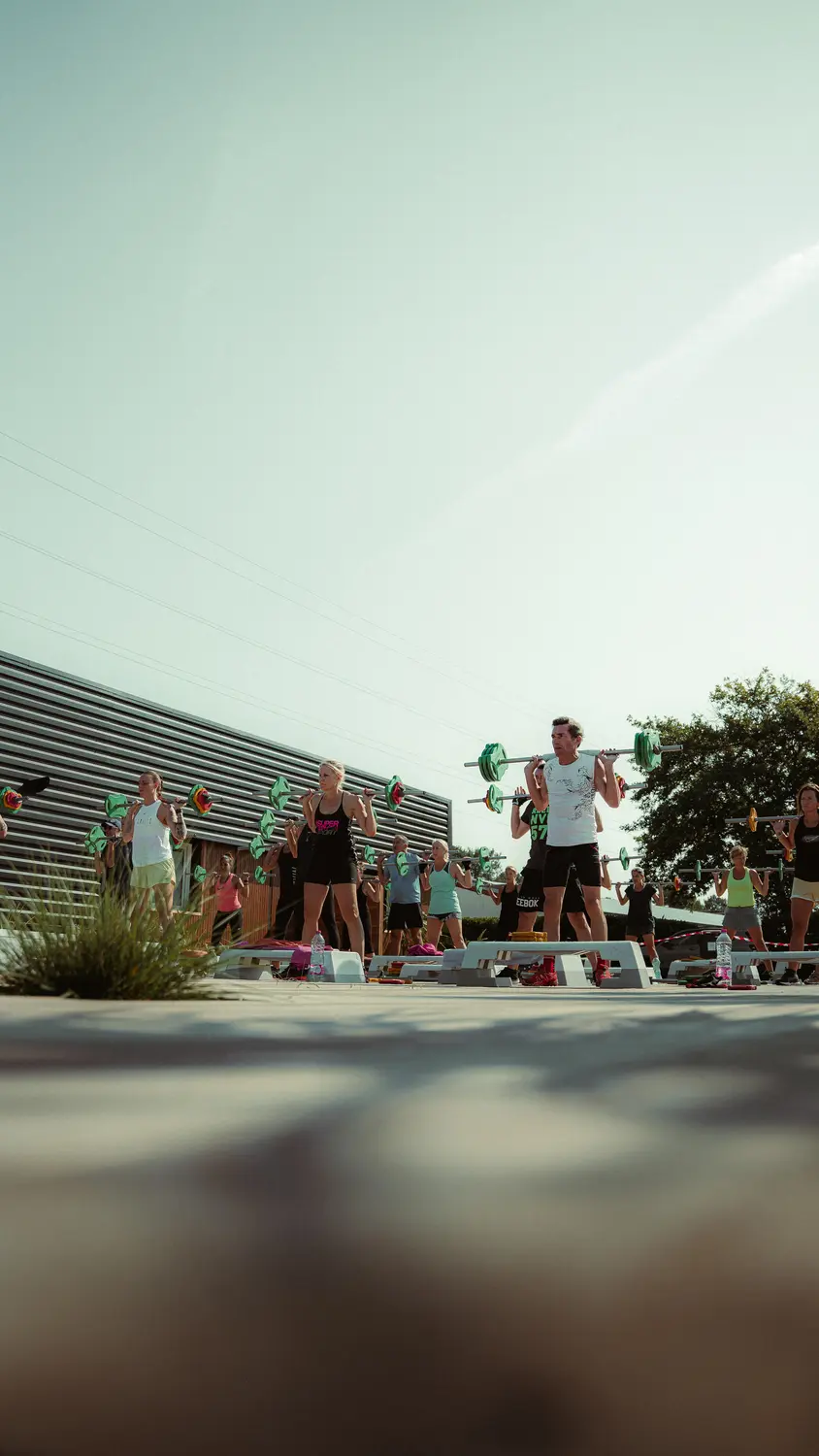 Groupe d'athlètes effectuant des squats avec des haltères verts en plein air. Cours de fitness intensif au soleil, coach au centre.