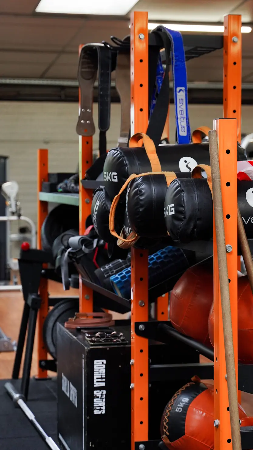 Rack de fitness orange rempli de matériel : sacs de lestage noirs 5KG, sangles SVELTUS et plyo box GORILLA SPORTS.