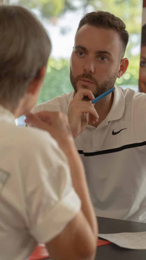 Gros plan d'un homme attentif en polo blanc (Nike) tenant un stylo bleu sur le menton, écoutant l'interlocuteur lors d'une consultation.