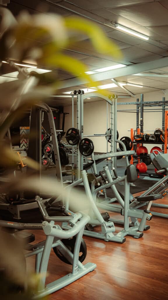 Équipement de musculation Matrix et rack de poids Jordan dans une salle de sport moderne bien éclairée, sol en bois, effet bokeh en premier plan.