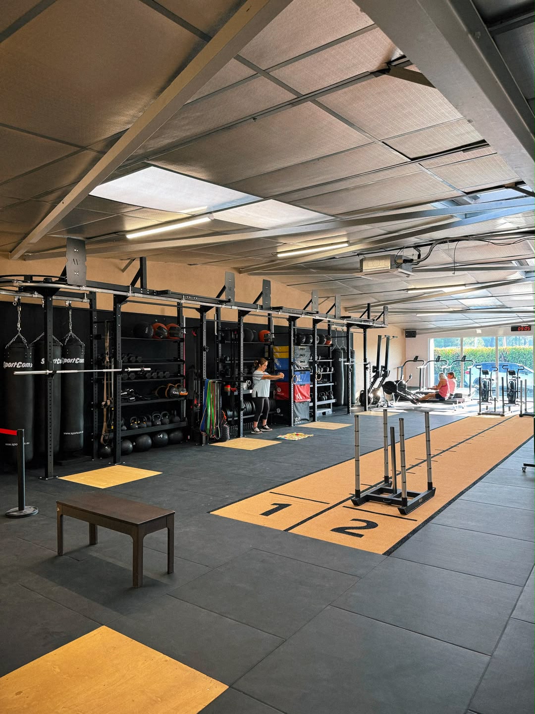 Salle de sport avec sacs SportCom, piste de luge, racks et zone d'entraînement fonctionnel pour CrossFit.